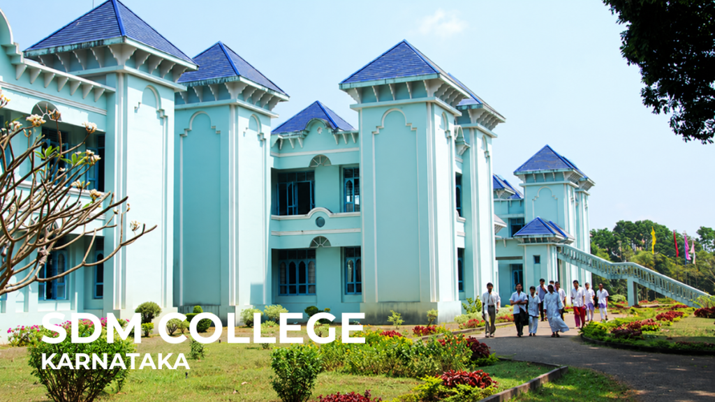 SDM College of Naturopathy and Yogic Sciences in Karnataka, India, with pale green buildings, blue tiled roofs, landscaped gardens and students walking along a campus path.